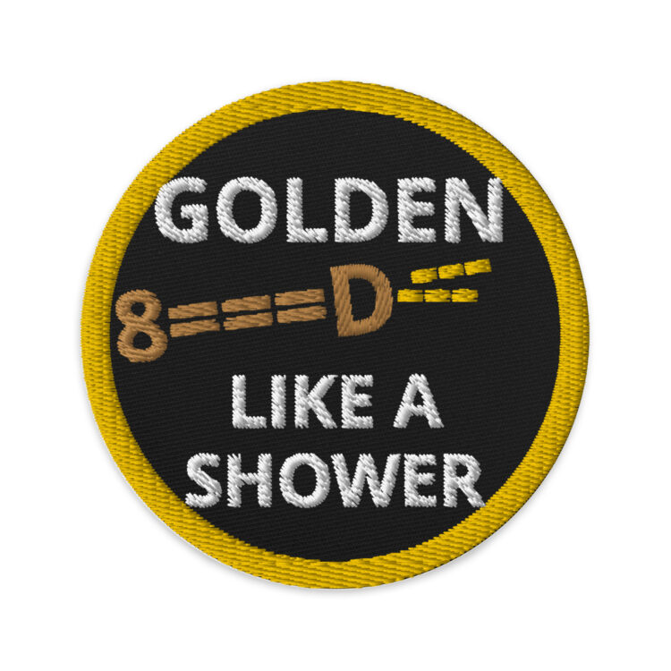 3 inch circle patch with a gold outline around a black background. With the white words "GOLDEN LIKE A SHOWER" written inside the circle with the word Golden being separated by the phrase by a typeface peeing penis. The penis being brown and the pee being yellow. denimandpatches