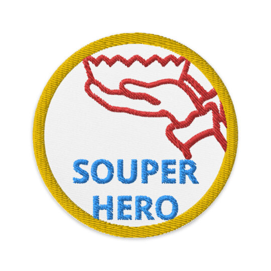 3 inch circle patch with a gold outline around white background. Centered is a pointed edge bowl with 2 hands and arms holding it up with the words "SOUPER HERO" beneath it. The words are a light blue color. denim and patches