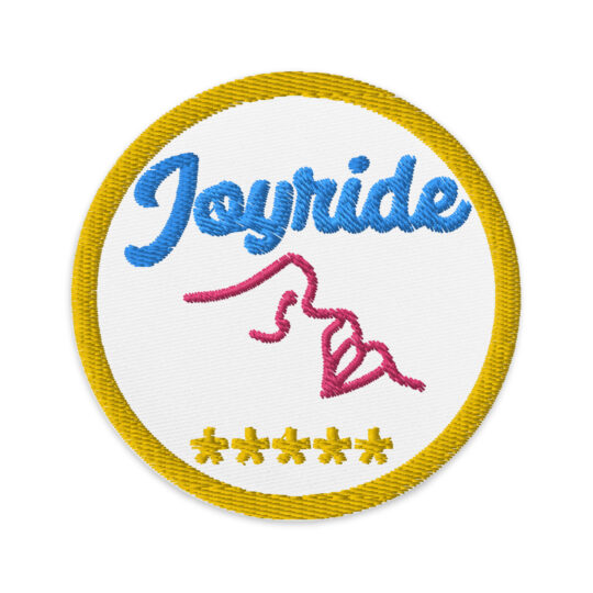 3 inch circle with a yellow outline around a white background. With the word "Joyride" written in light blue above the outline of a pair of lips and a nose in hot pink. Underneath said lips are 5 yellow asterisk. denimandpatches