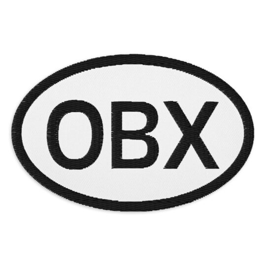 3 inch oval shaped patch with a black outline around a white background. With the letters "OBX" centered in the oval. denim and patches