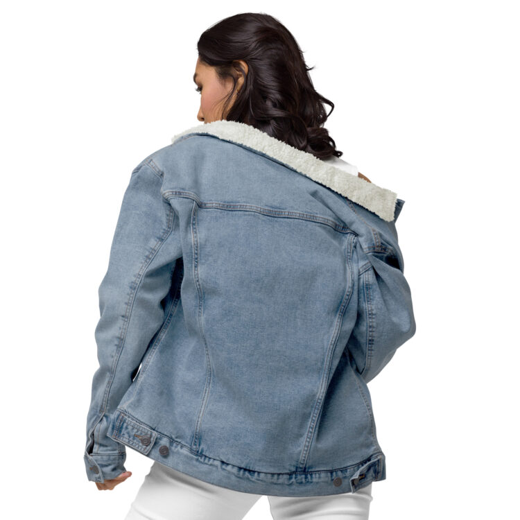 The back of a young female model wearing white clothes underneath the light blue denim sherpa lined jacket. The jacket featuring aged-brass buttons along the bottom to help with wind going up the jacket. The jacket also features some seams along the back of the jacket. denimandpatches
