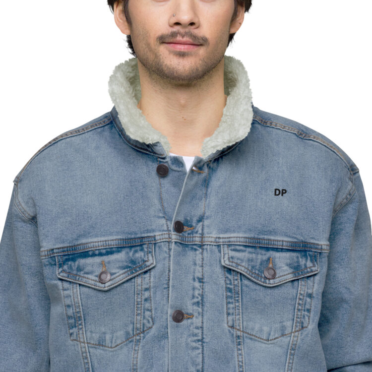 Front shot of brunette male model. Modeling our sherpa-lined denim jacket. Showing off the fluff on the inside around the neck and the 2 frockets on the jacket. That are held closed by antique brass buttons with the letters "DP" in bold black lettering above the left frocket. denimandpatches